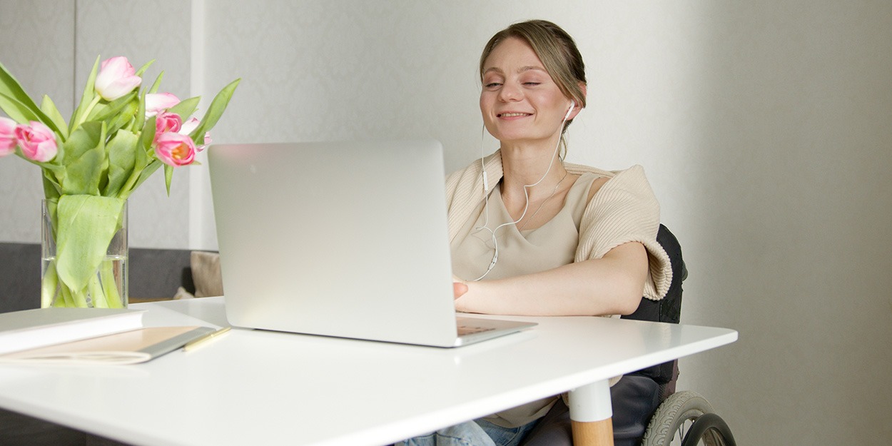 Young disabled woman in her 20s sitting at a table on a laptop, smiling